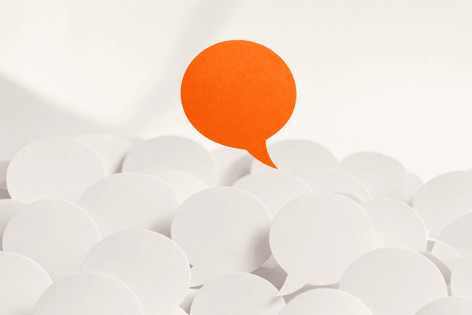 One orange paper speech bubble rising above a sea of plain white ones: the single answer named out of many.